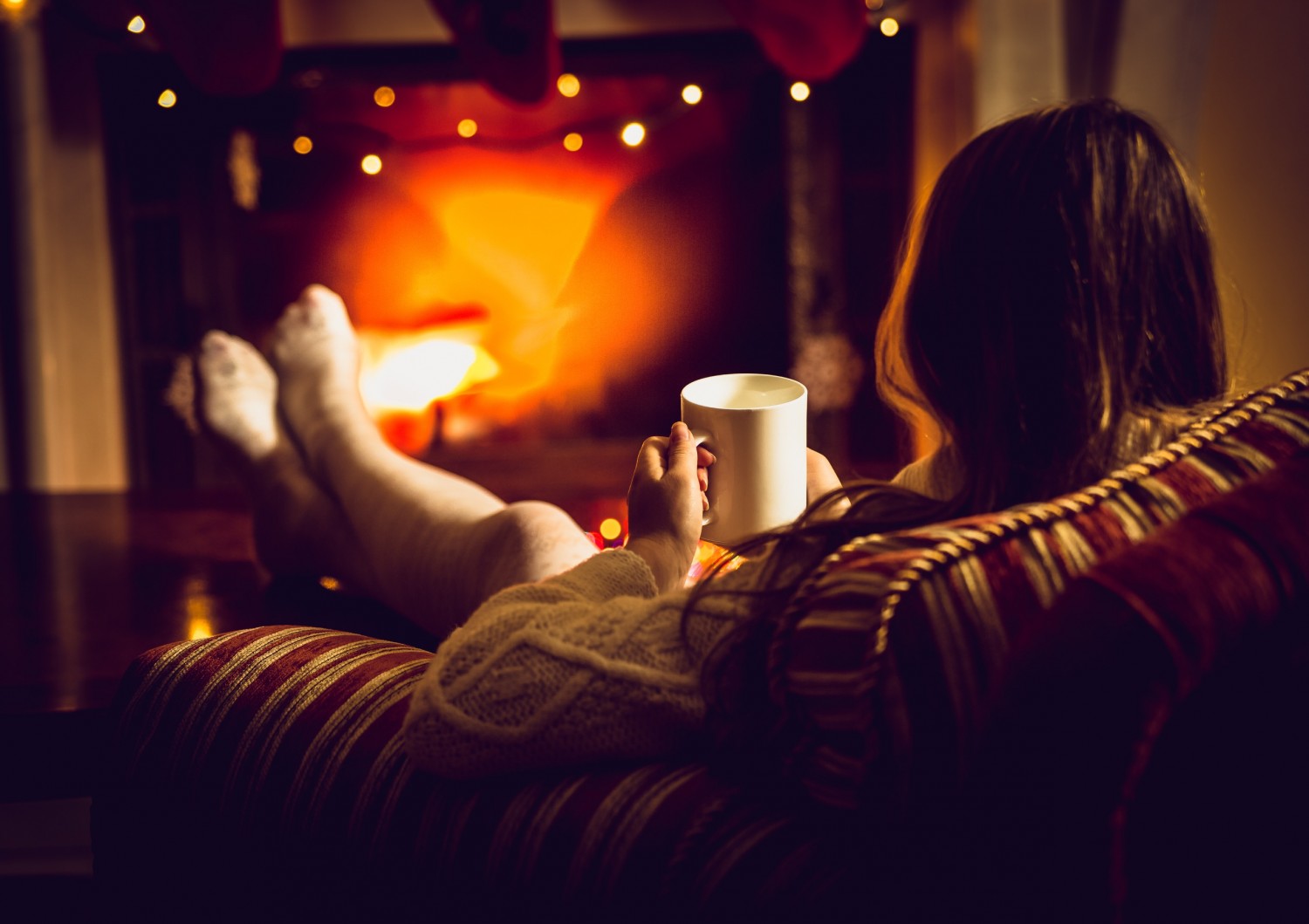 BM_Toned photo of woman warming up with hot tea at fireplace_73067947