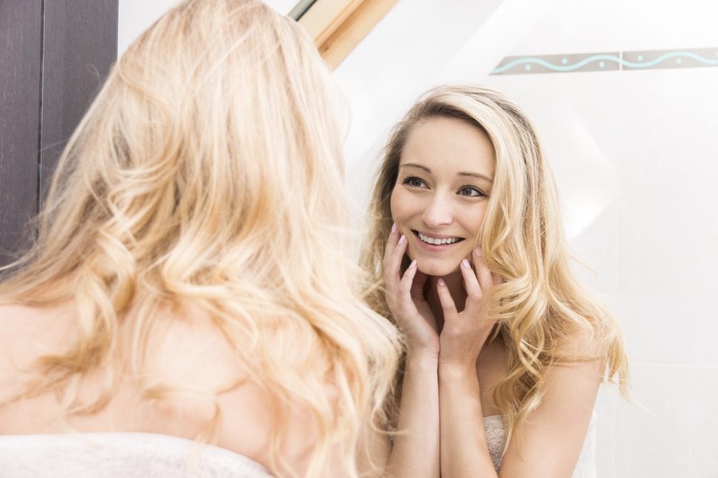 bm_young-blond-woman-looking-at-self-in-mirror_101550922