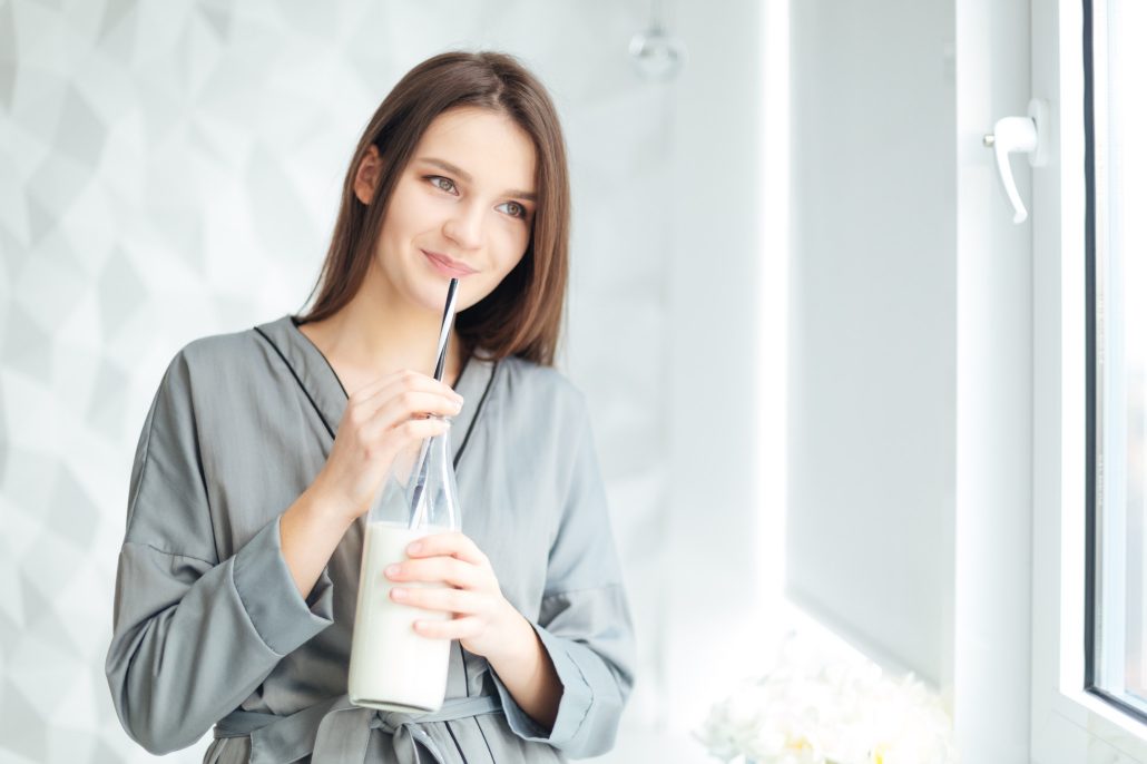 BM_Happy attractive young woman in grey bathrobe drinking milk_110761826